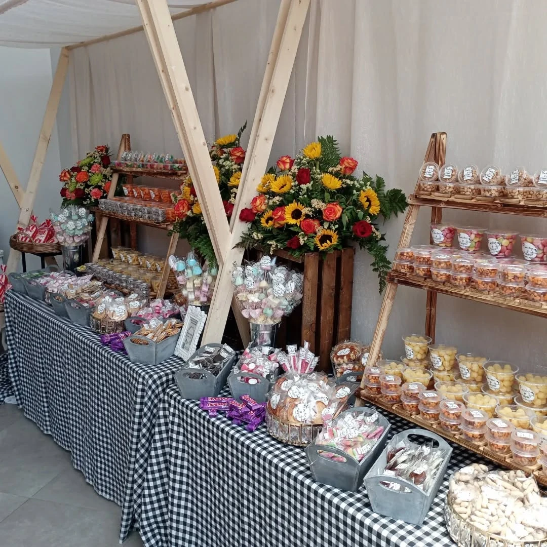 Mesa dulce con chucherías, galletas y centros de girasoles y rosas sobre mantel de cuadros